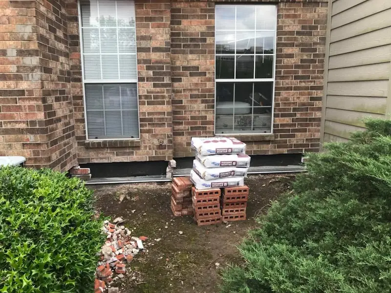 Brick and mortar repair at the base of an exterior wall