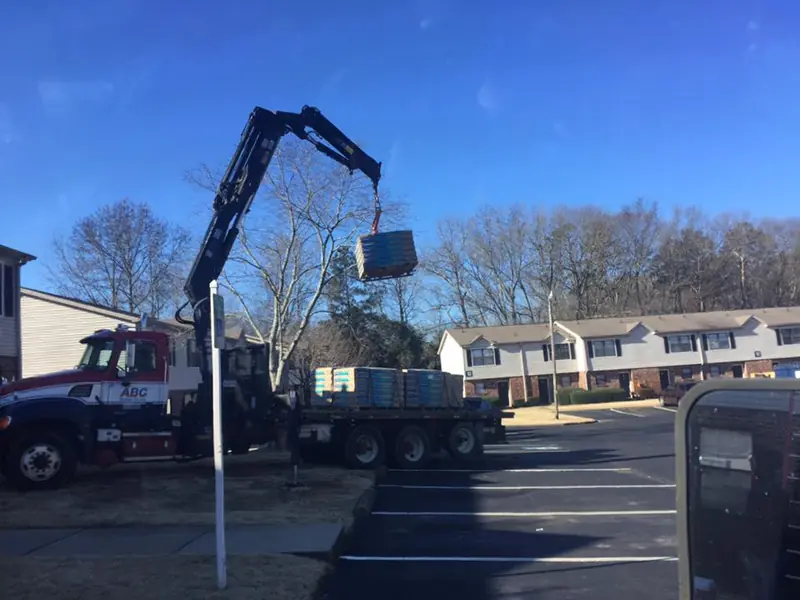 Boom truck lifting shingle bundles to the roof of an apartment complex